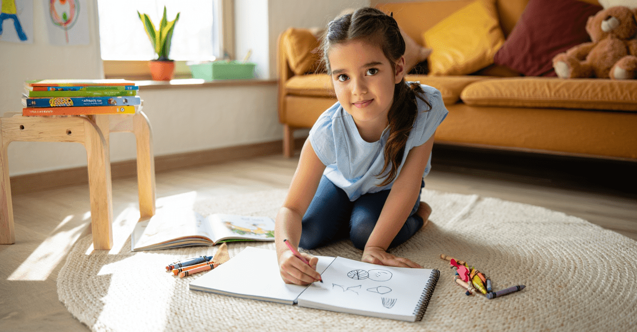 Child drawing in a sketchbook with crayons on a rug.